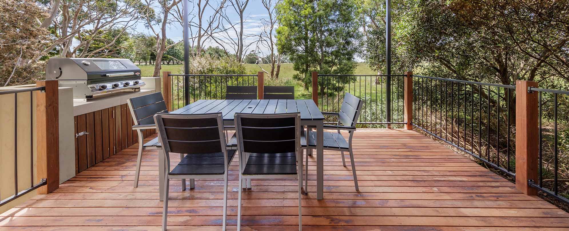 A wood patio with a table and 6 chairs, grill, and railing in a Club Wyndham Phillip Island 3-bedroom suite.