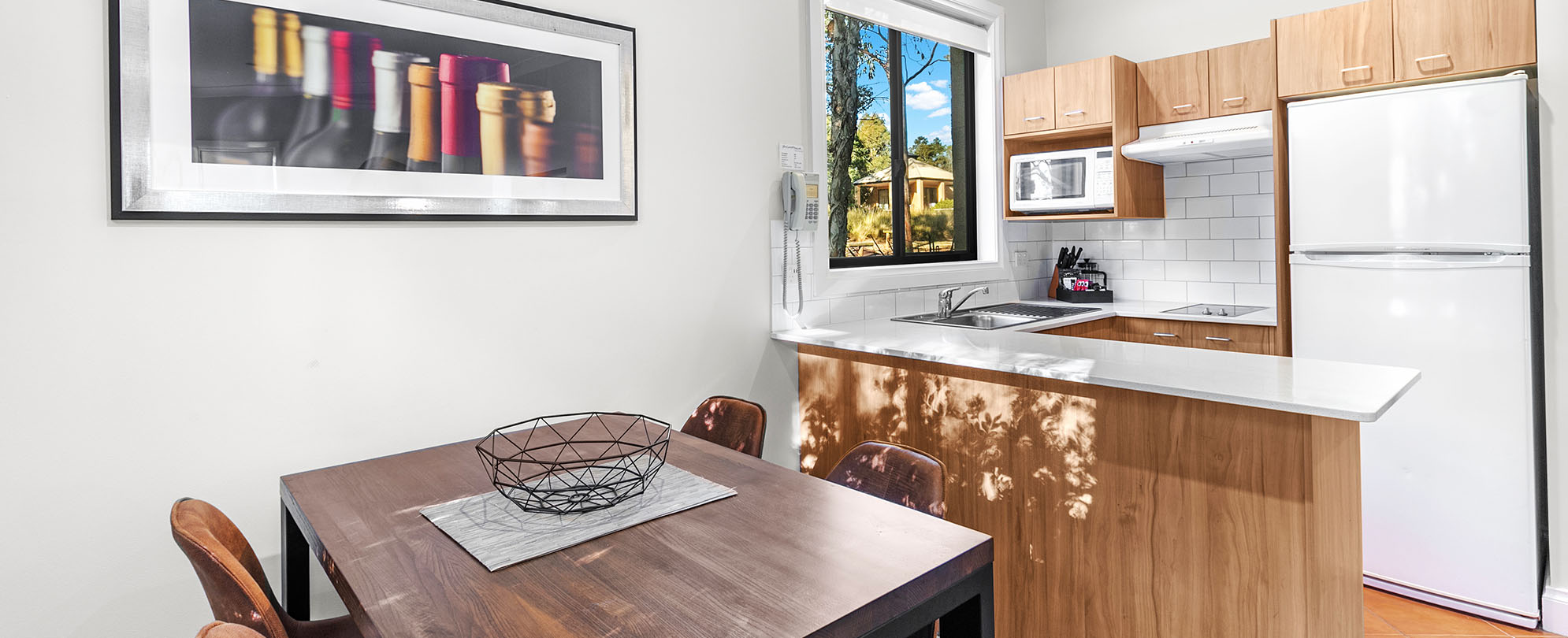A 4-person dining table and kitchen with a full fridge, microwave, and stove in a Club Wyndham Pokolbin Hill 2-bedroom suite.