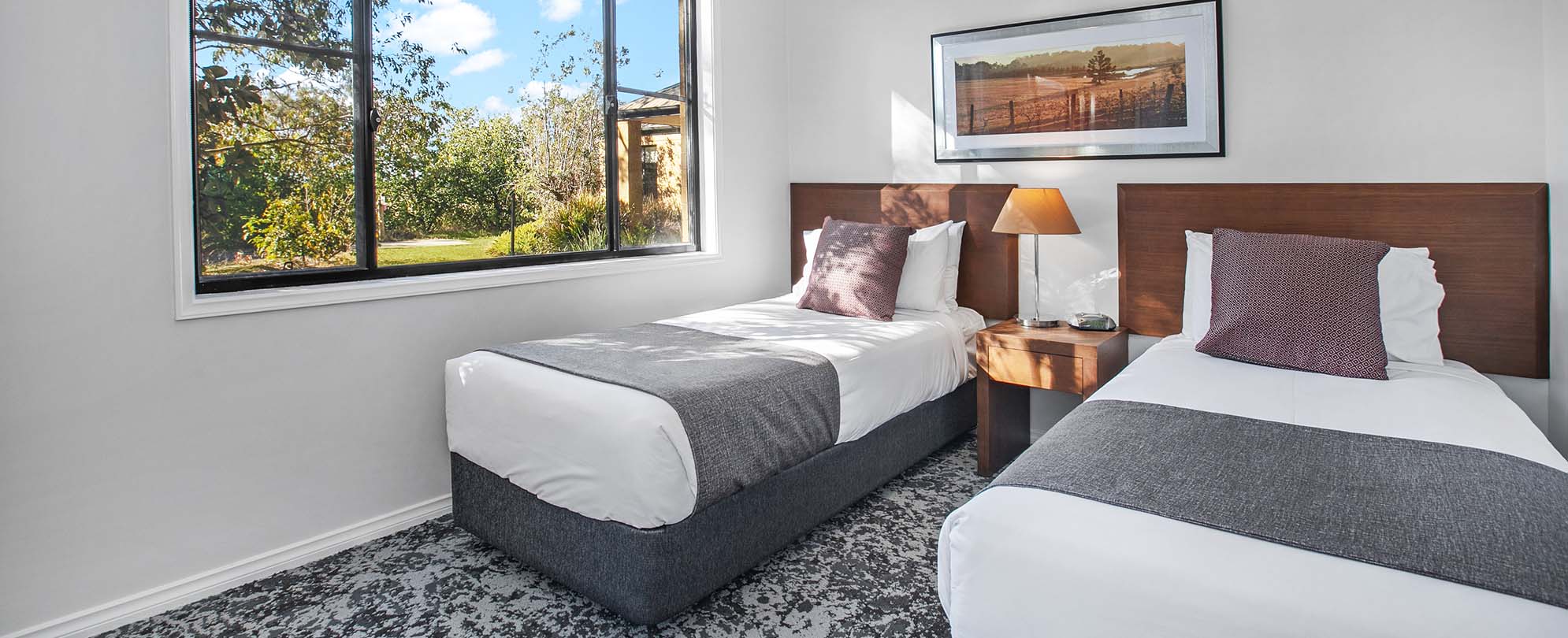 A bedroom with two twin beds, large window, and a nightstand with a lamp in a Club Wyndham Pokolbin Hill 2-bedroom suite.
