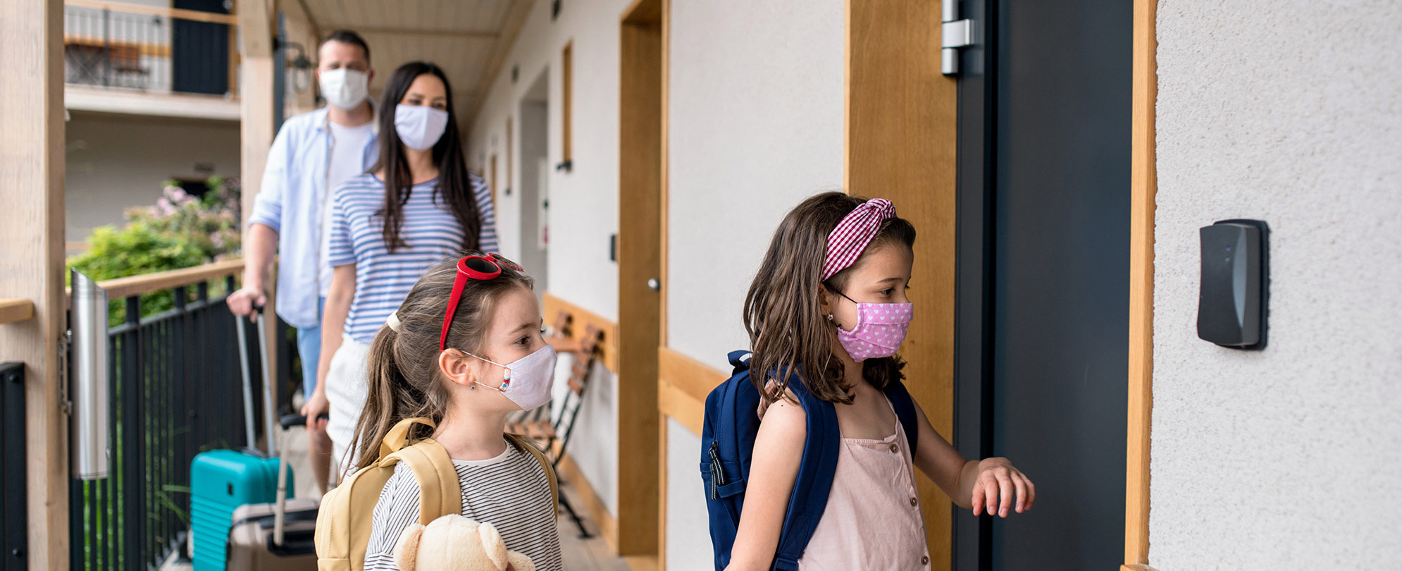 A mom, dad, and two daughters wearing masks covering their mouth and nose enter their WorldMark by Wyndham resort suite. 