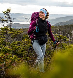 A woman wearing a headband and backpack uses trekking poles to hike in the mountains of a National Park.