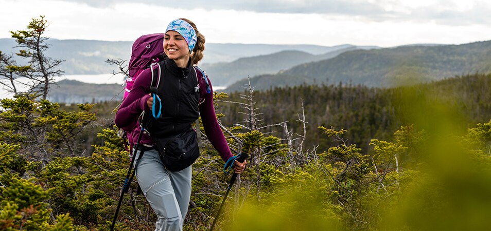 A woman wearing a headband and backpack uses trekking poles to hike in the mountains of a National Park.