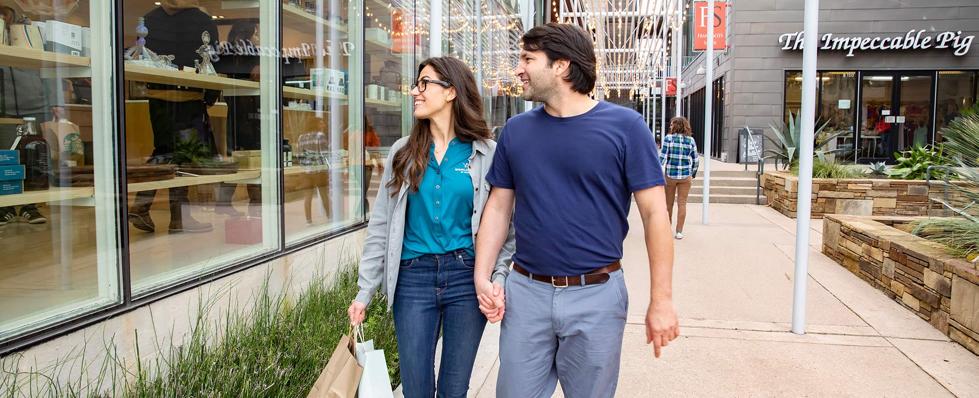 A couple holding hands as they walk together in a shopping mall. 