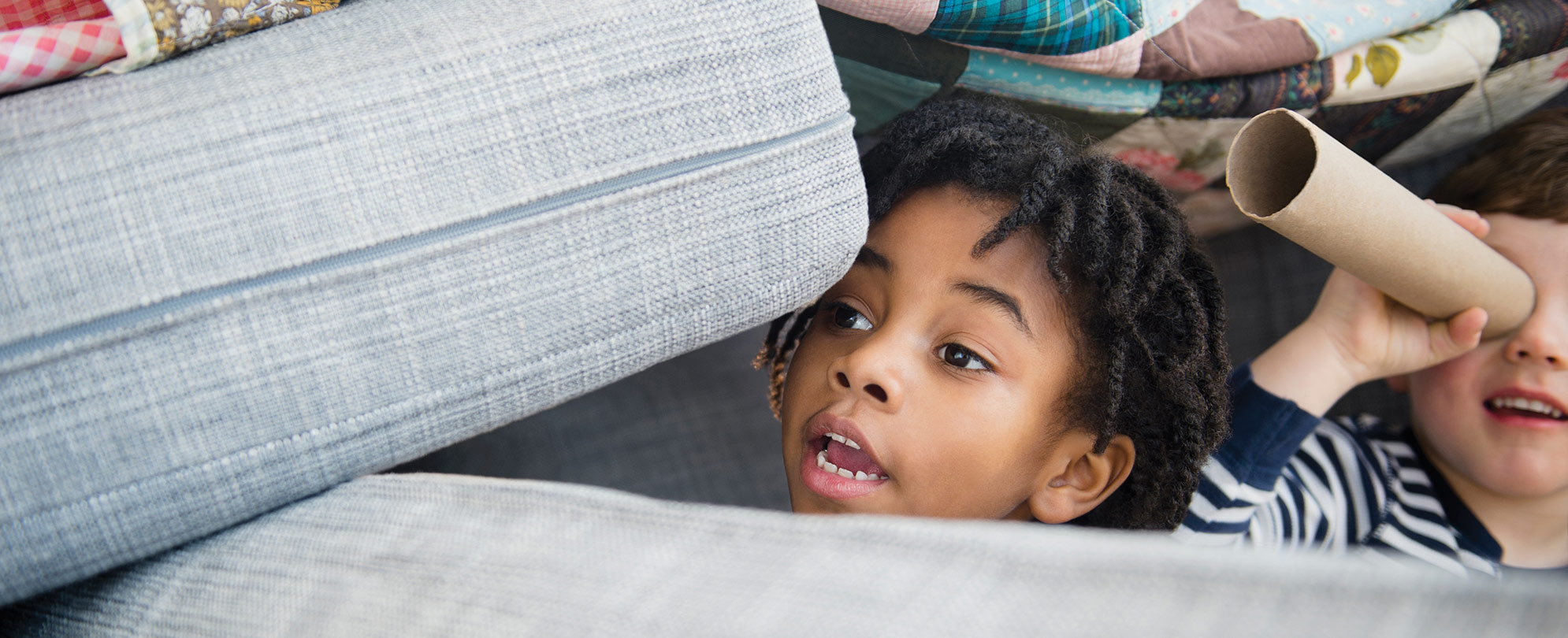 Two kids playing in a pillow fort.