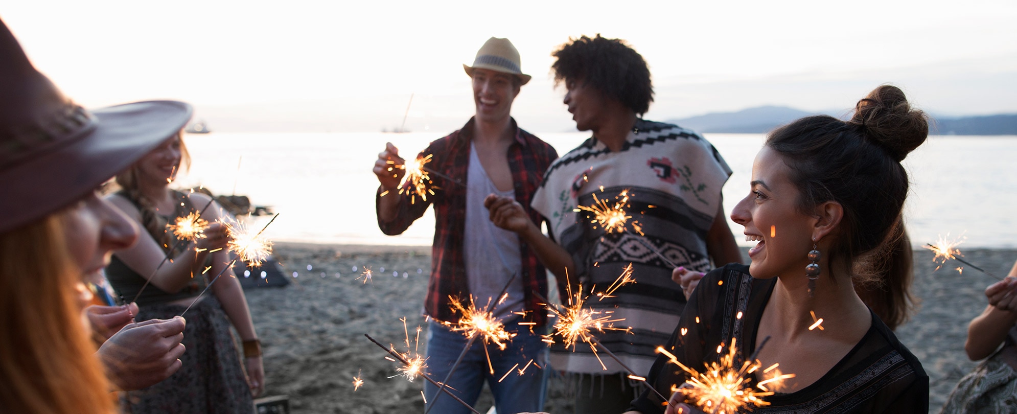 A group of friends all gathered together on a beach holding lit sparklers. 