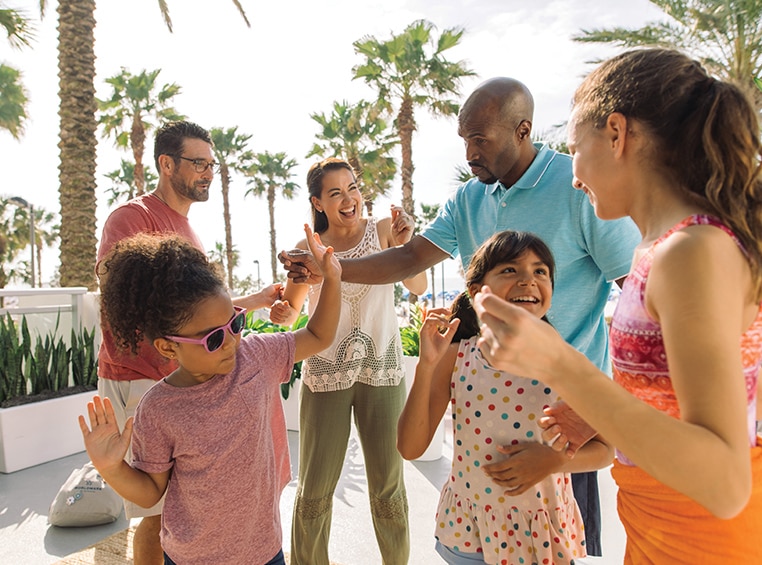 3 adults and 3 young kids smiling and dancing at a WorldMark resort with palm trees in the background.