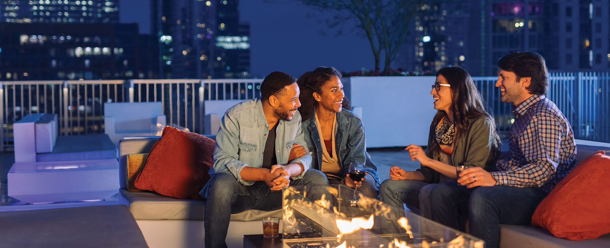 Two couples sitting and talking around a glass fire pit at the rooftop deck of a WorldMark resort.