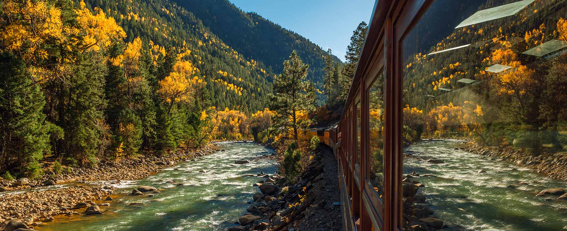 A train traveling through the mountainside with a flowing river beside it.