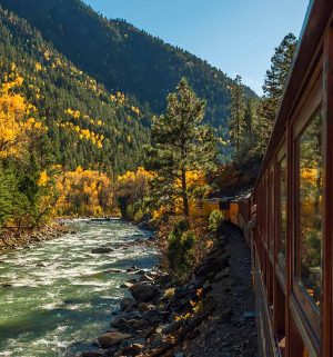 A train traveling through the mountainside with a flowing river beside it.