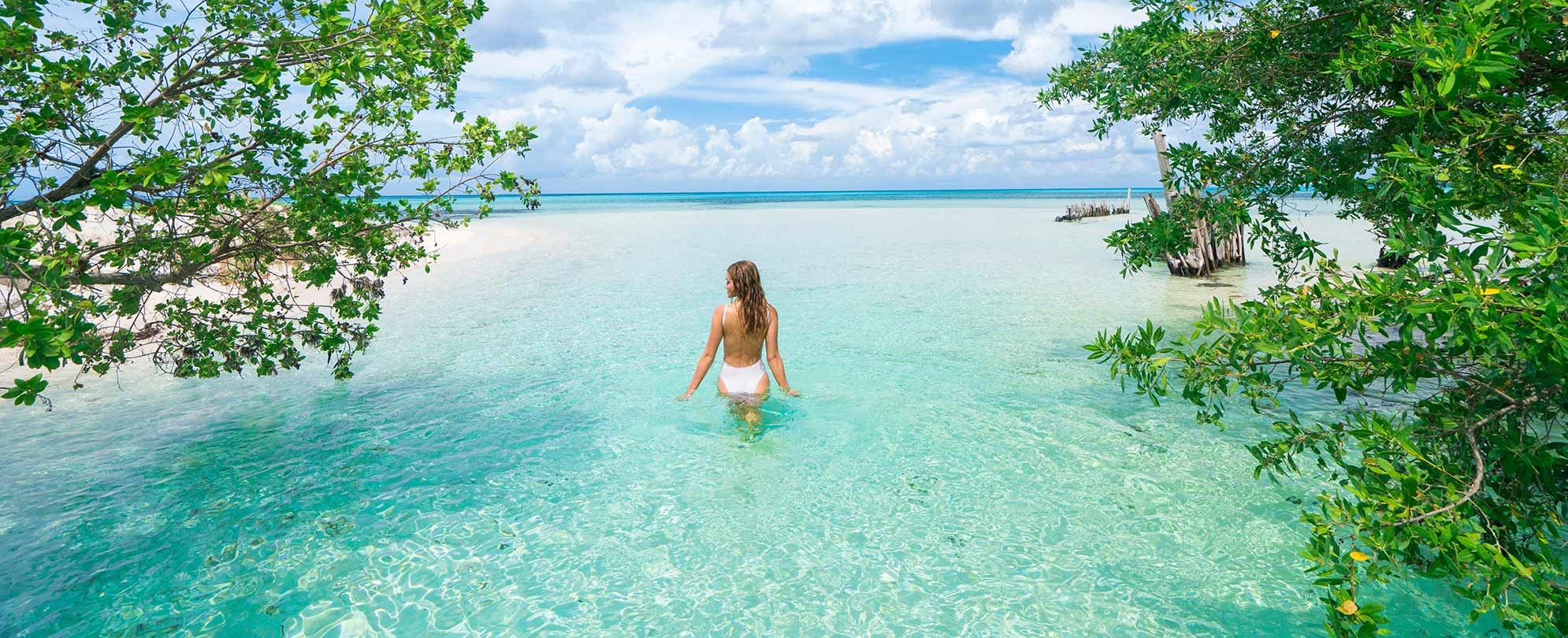 A woman wading in clear, calm water with blue skies in the Western Caribbean.
