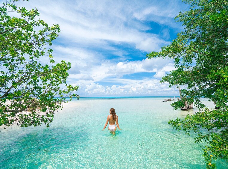 A woman wading in clear, calm water with blue skies in the Western Caribbean.
