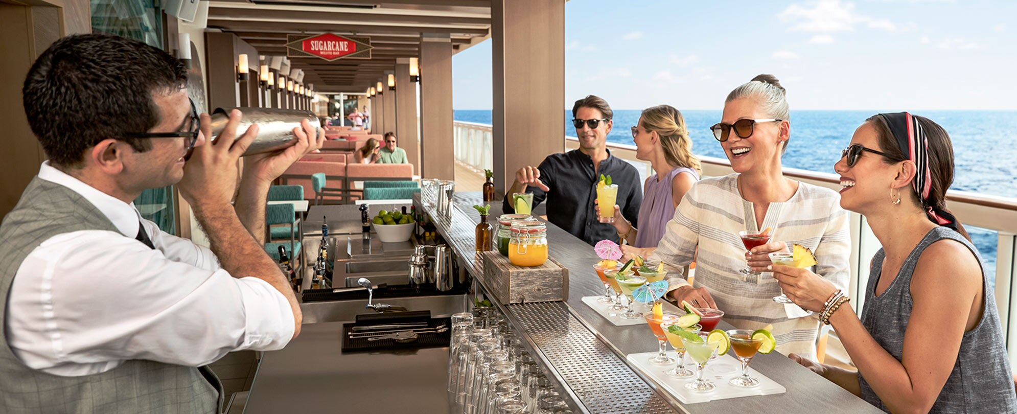 Adults sit at a cruise ship bar enjoying cocktails while a bartender mixes a drink on their Mexican riviera cruise.