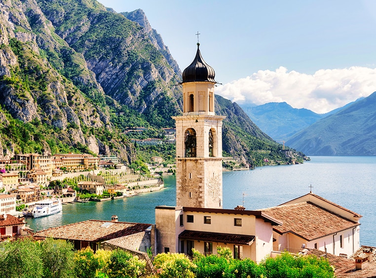 A bell tower in Limone sul Garda, a town in Lombard, Italy, with mountains, buildings, and Lake Garda in the background.