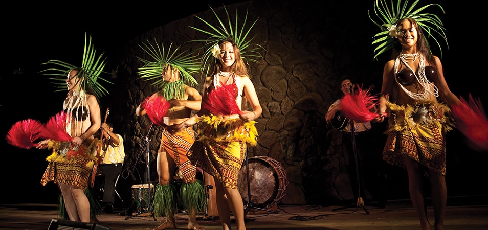 Luau performers wearing palm headdresses, coconut shells, and skirts. 