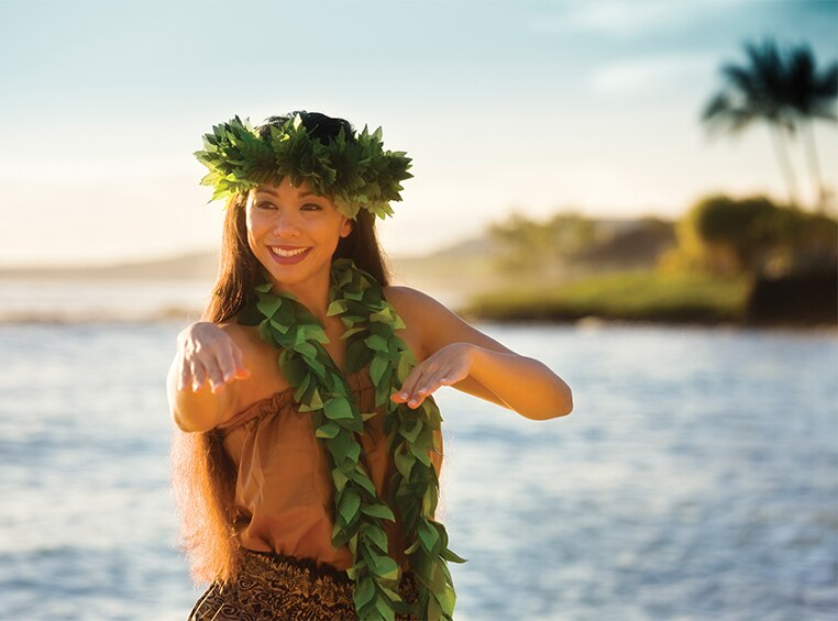 A smiling Hawaiian luau performer with the ocean in the background at the Royal Kona Luau.