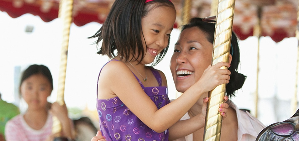 A mother is holding on to her daughter who is riding a horse on a carousel.