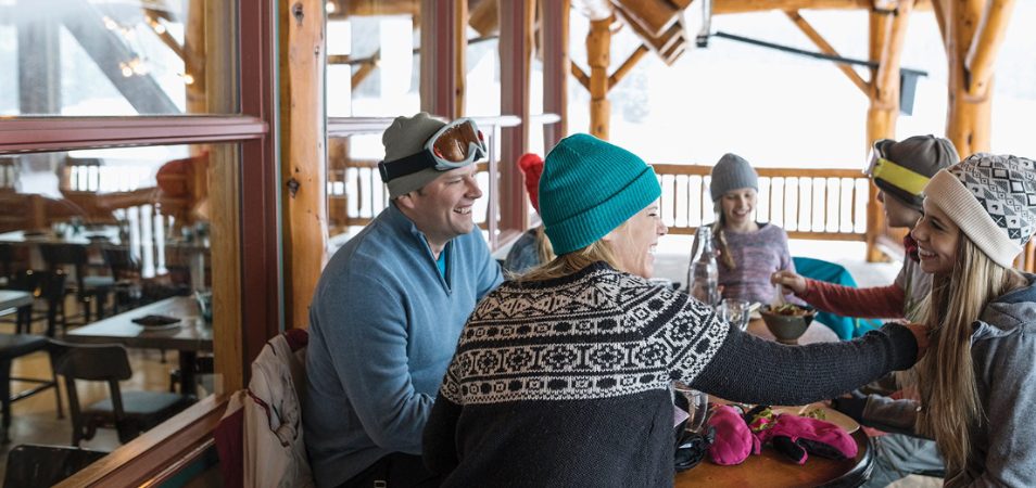 A family in winter clothes and ski gear sit around a table on a porch at a WorldMark by Wyndham resort.