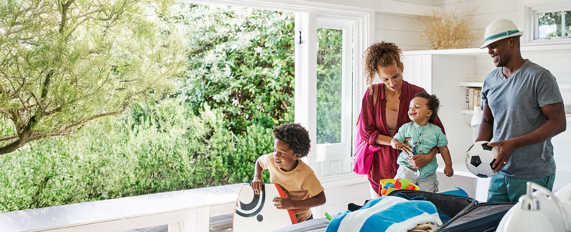 A family preparing for a day out, with two children holding toys, surrounded by greenery and a bright, airy room.