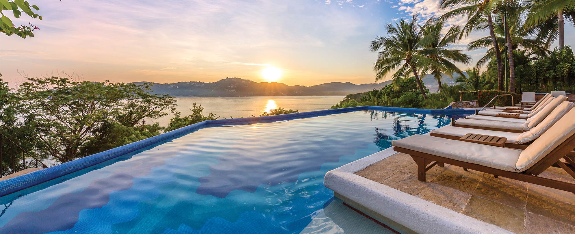 Oceanfront pool surrounding by palm trees and lounge chairs at WorldMark Zihuatanejo in Mexico.