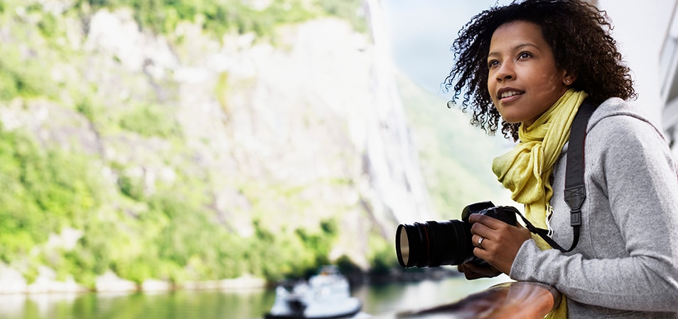 Woman holding a camera and looking out at the view from a river cruise balcony. 
