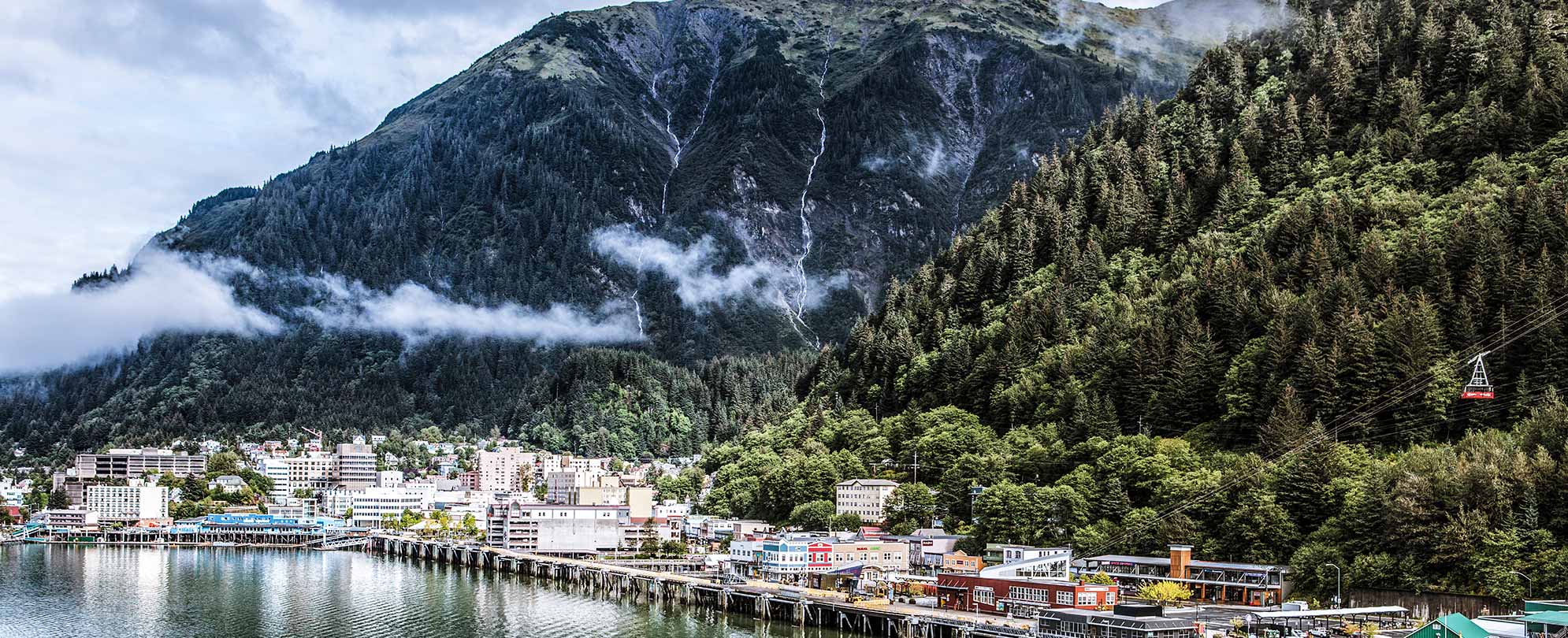 A large mountain with a small village beneath it overlooking the water on an Alaskan cruise with Worldmark by Wyndham. 