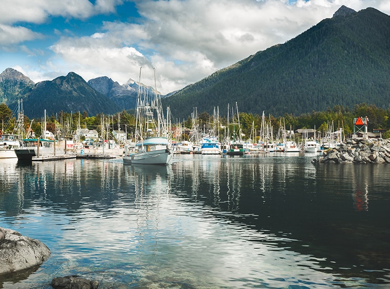 Sail boats in a harbor surrounded by mountains in Alaska.