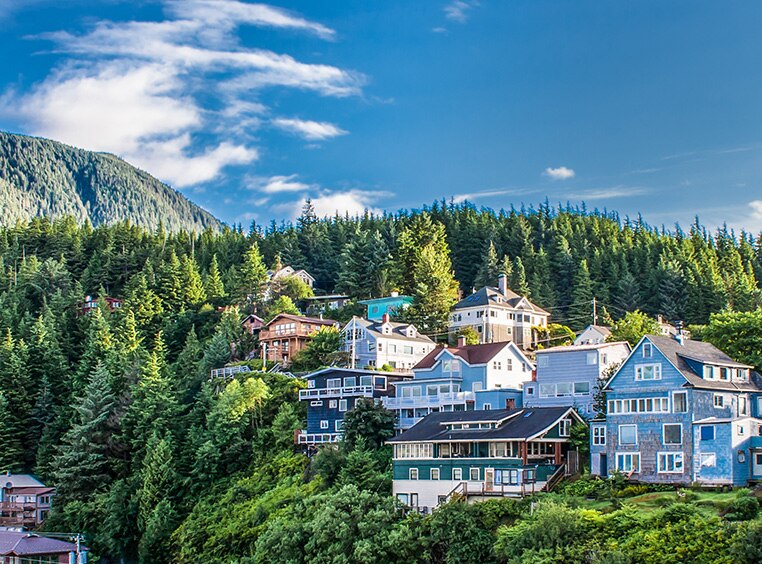 Multiple houses on a hill surrounded by pine trees and mountains in Ketchikan, Alaska.