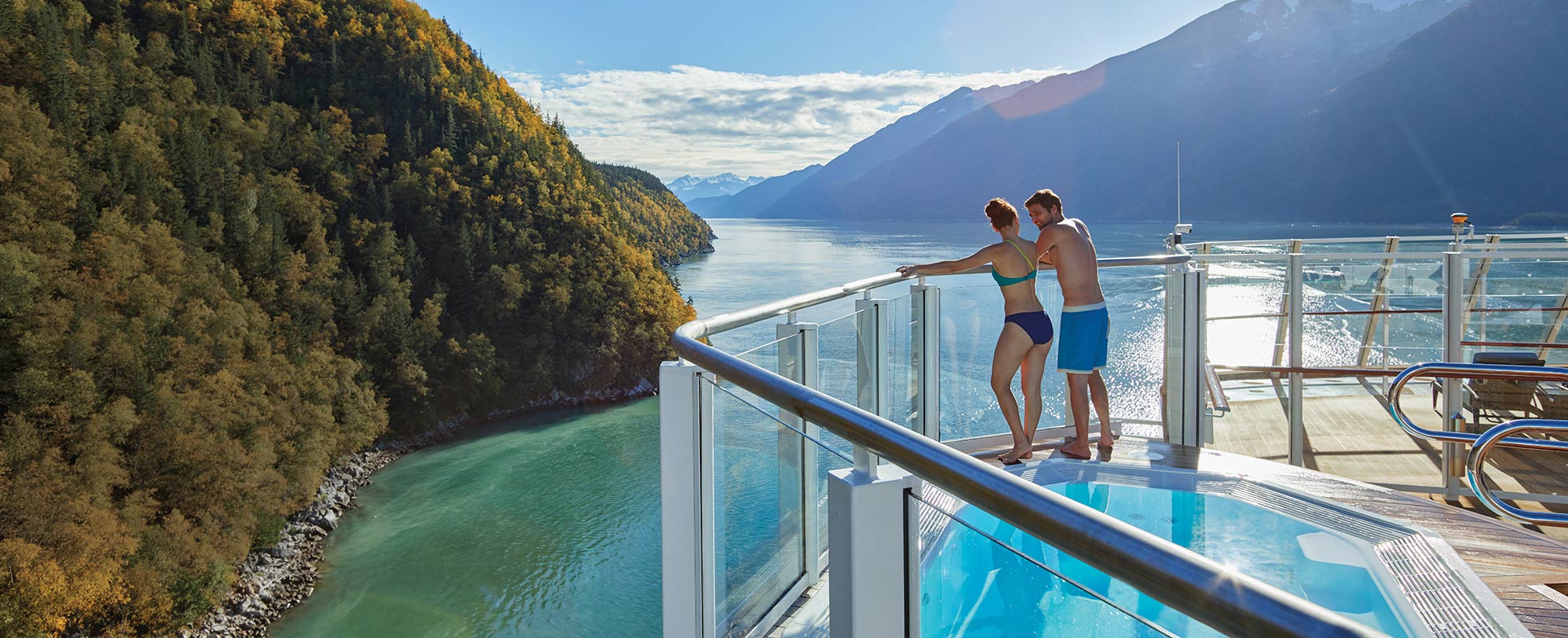Couple leaning against balcony railing while overlooking a lake and Mountains in the Norwegian Cruise.