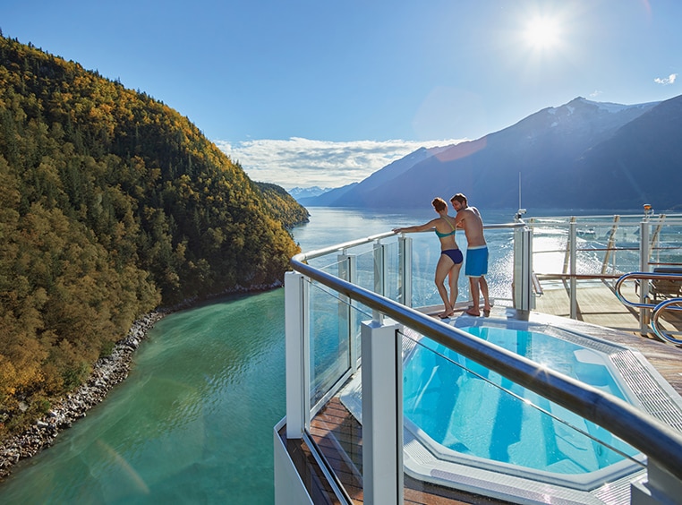 Couple leaning against balcony railing while overlooking a lake and Mountains in the Norwegian Cruise.