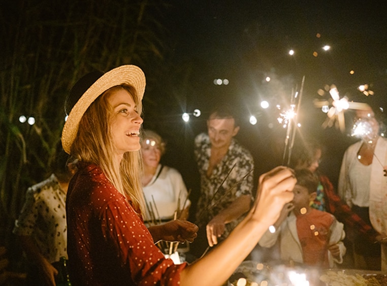 A woman holding a sparkler in her hand and smiling. 