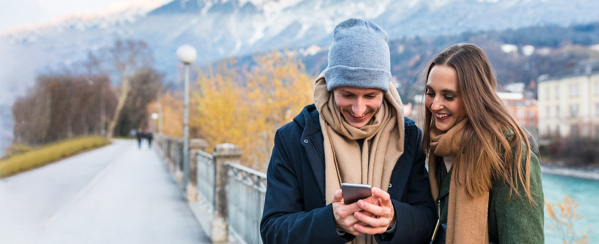 Two adults standing outside in a park smiling at a phone. 