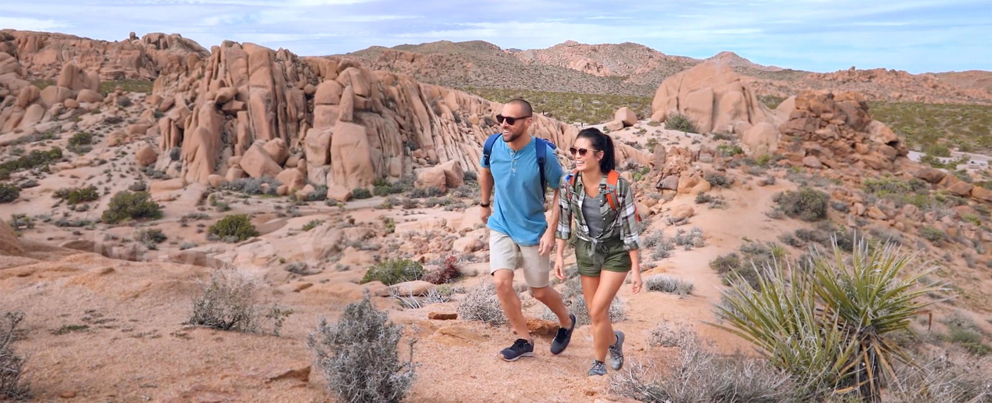A couple taking a hike up a desert trail surrounded by red rocks. 