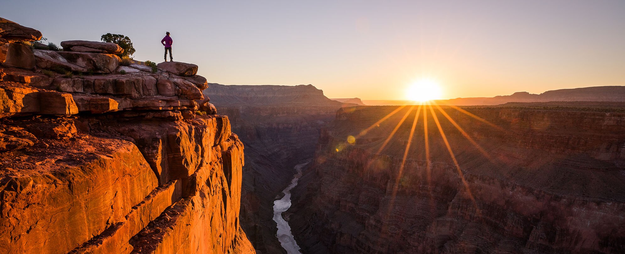 A man, standing on the top of the Grand Canyon looking at the sunset.