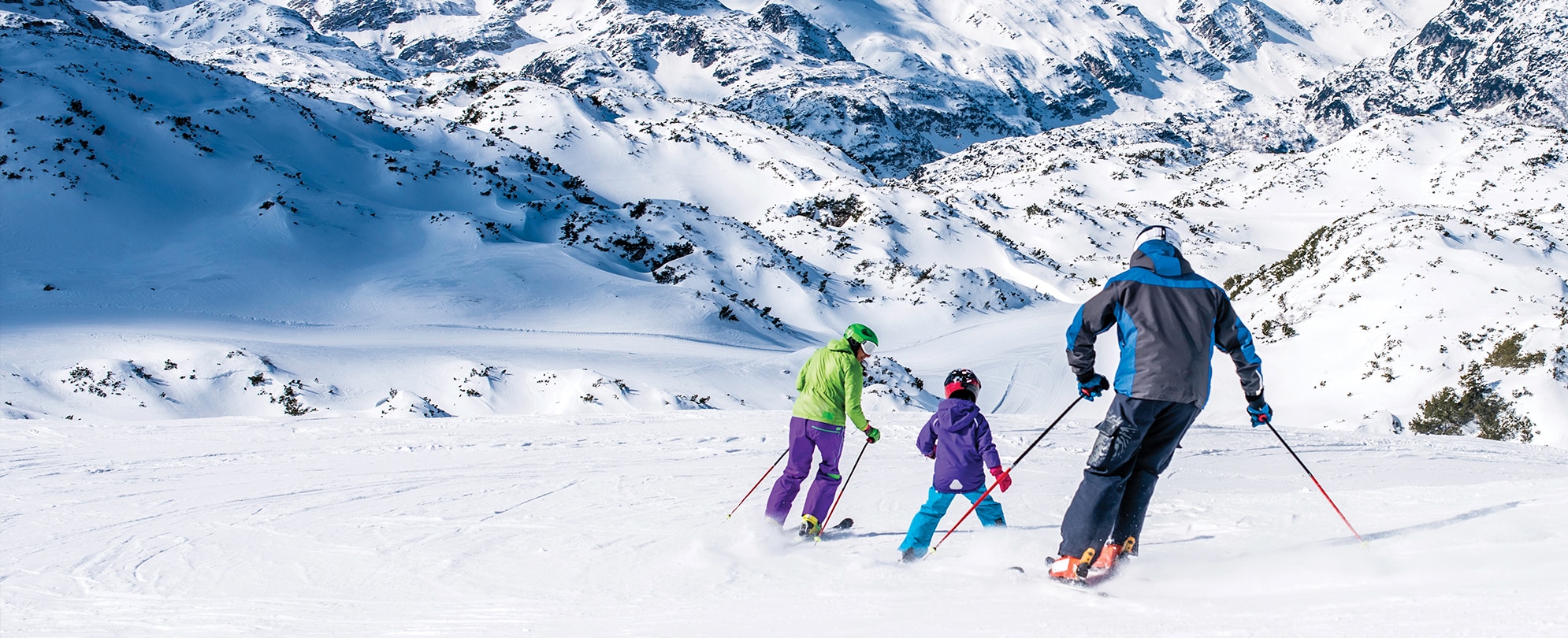 A father and two children wearing winter gear skiing on a snowy mountain. 