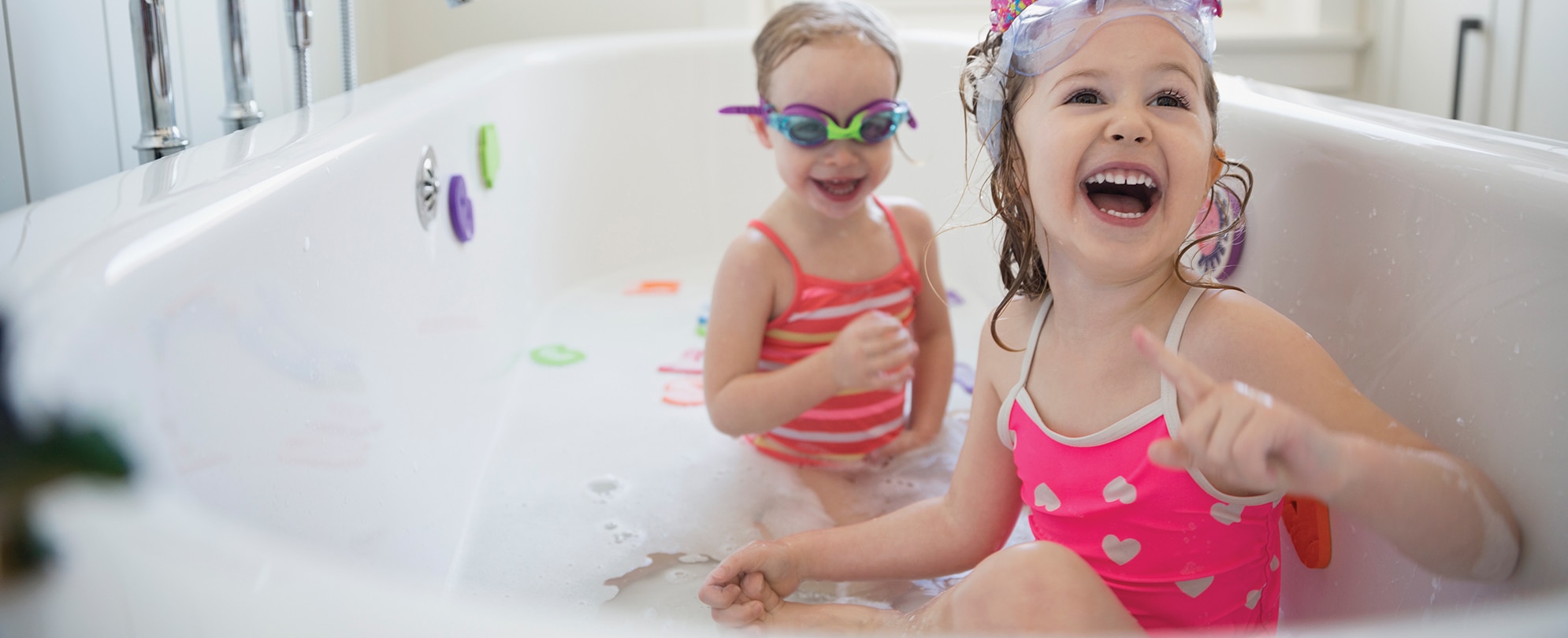 Two smiling young girls wearing goggles and swimsuits play in a bubble bath at a WorldMark by Wyndham resort.