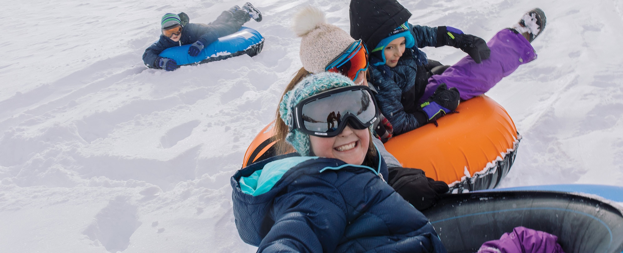 Four kids riding down a mountain on snow tubes.