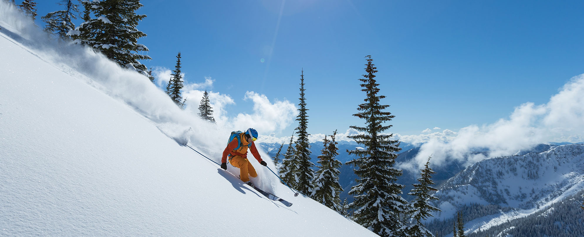 A skier going down a slope with mountains and tall evergreen trees in the background in Whistler, Colorado.