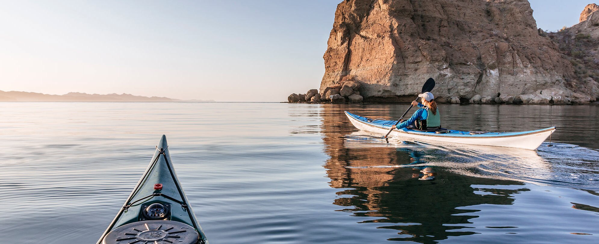 Two kayakers, paddling past sea cliffs in Baja, Mexico.