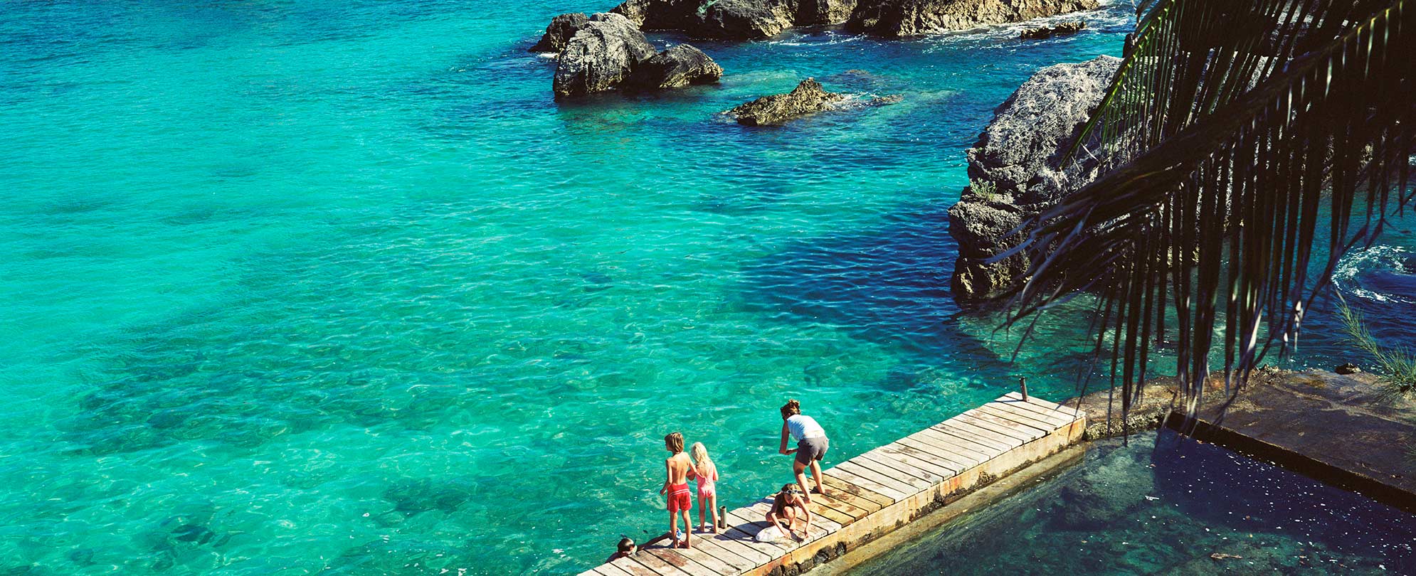 A family of four, looking into the clear blue ocean water from a pier in Bermuda.