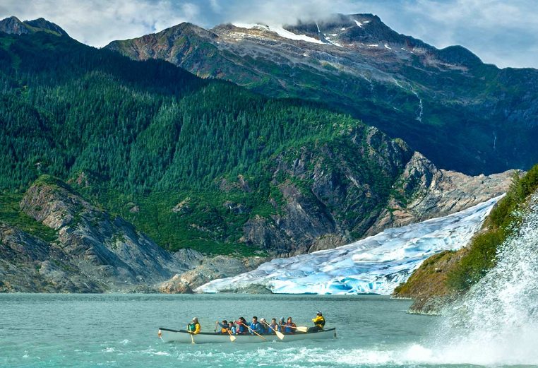A large group of people canoeing by a waterfall in Alaska.