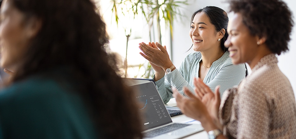 2 smiling women sit around a table looking off and clapping.