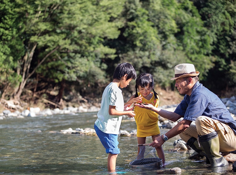 Two kids and their father with their feet in the water looking at something in their father's hand.