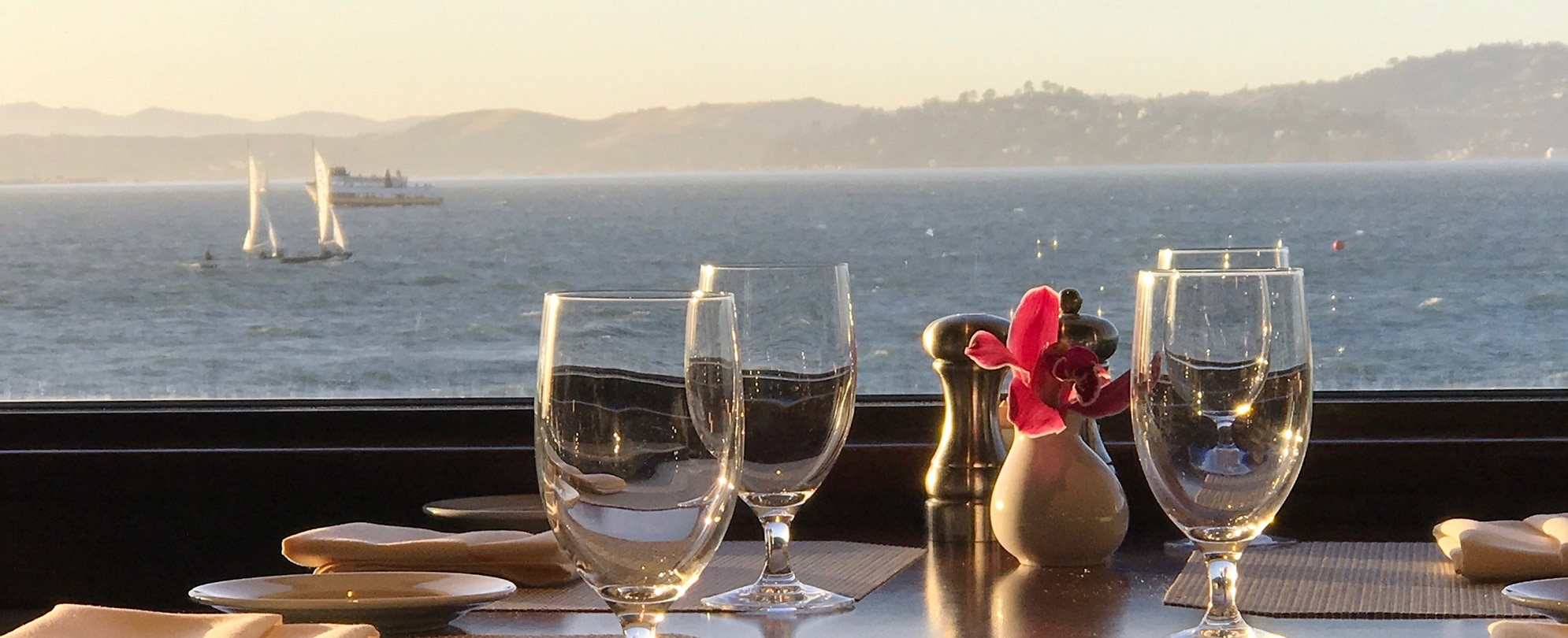 View from inside a waterfront restaurant of set table with four glasses overlooking the San Francisco Bay..