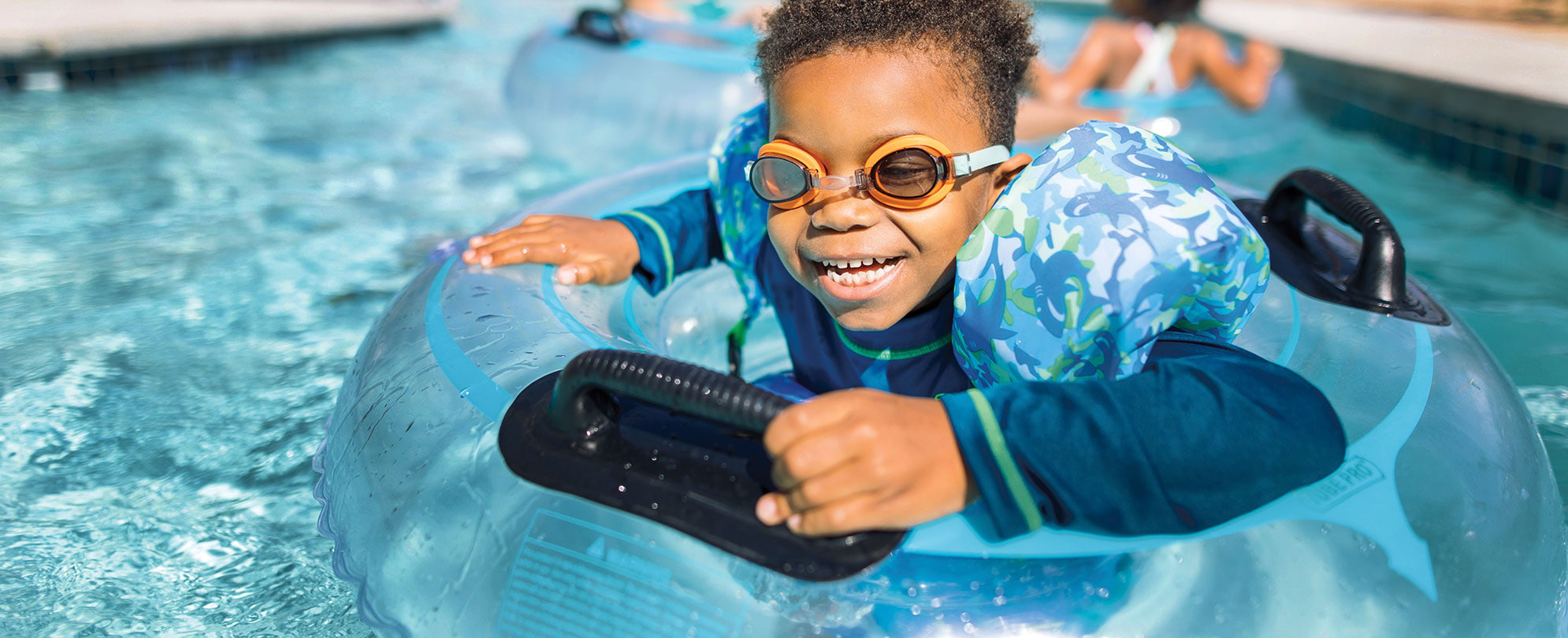 A young boy wearing goggles smiles while floating in an inflatable tube at a WorldMark by Wyndham resort pool.