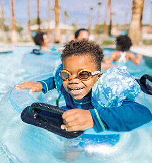 A young boy wearing goggles smiles while floating in an inflatable tube at a WorldMark by Wyndham resort pool.