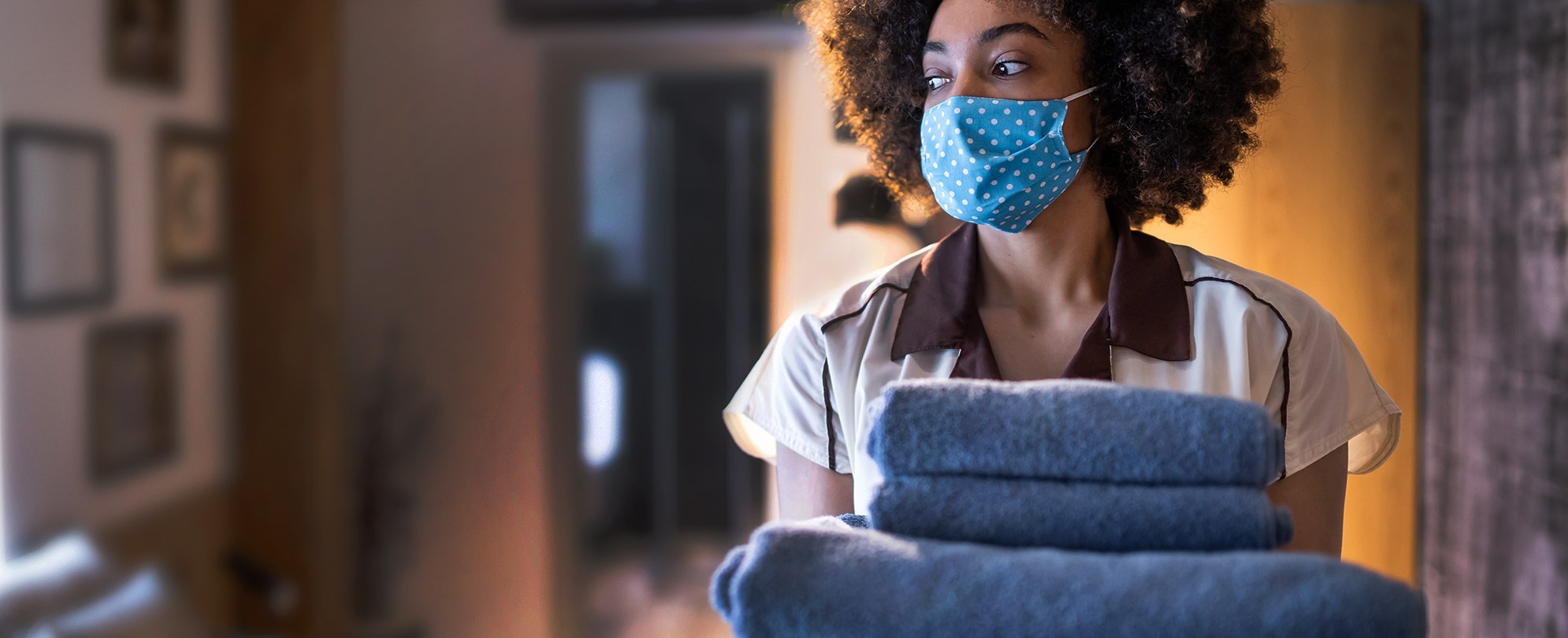 A female WorldMark by Wyndham employee wearing a medical mask and gloves holds a stack of blue towels.