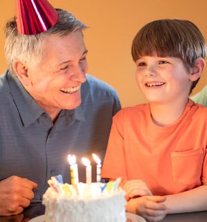 A young boy sits between two smiling fathers in front of a decorated birthday cake with candles.