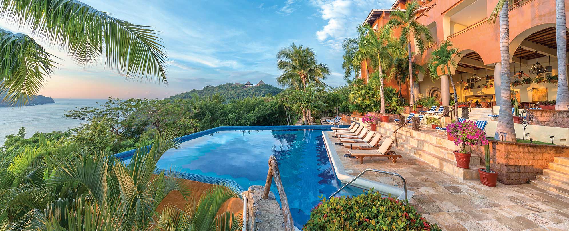Worldmark resort pool with view of the ocean and mountains surrounded by tropical plants in Zihuatanejo, Mexico.
