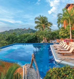 Worldmark resort pool with view of the ocean and mountains surrounded by tropical plants in Zihuatanejo, Mexico.