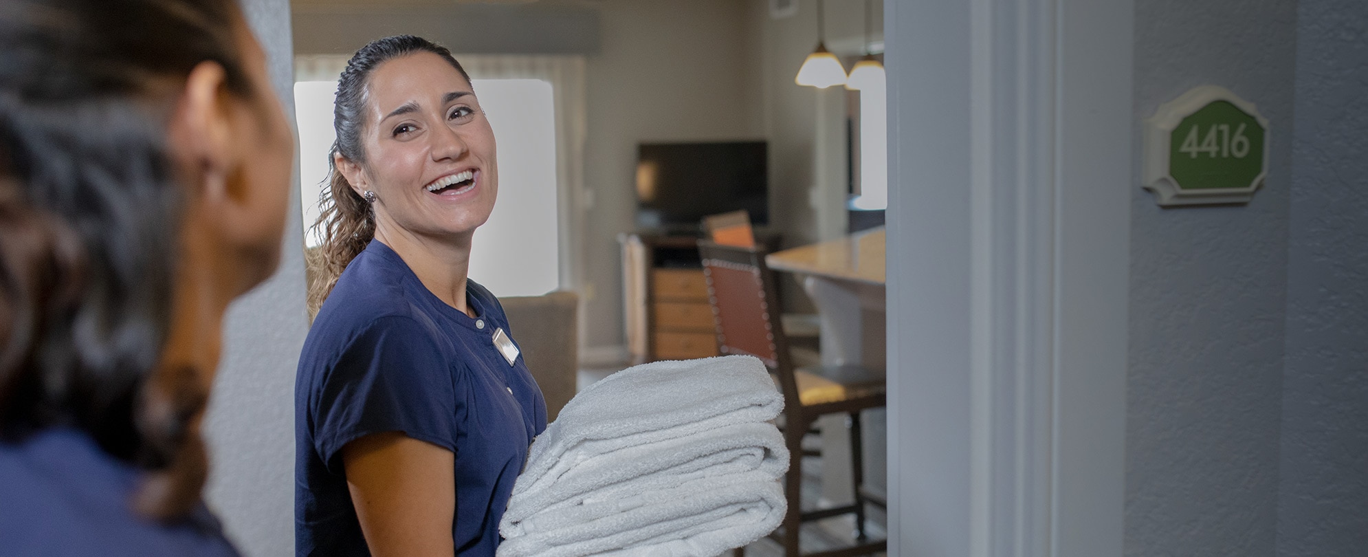 A smiling Club Wyndham employee holds a pile of towels as she enters a resort suite.